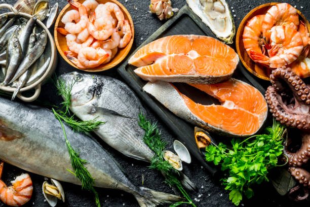 Fresh salmon steak with a variety of seafood and herbs. On black rustic background